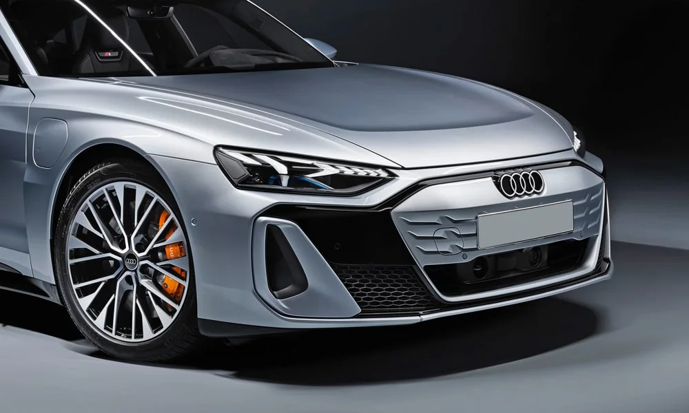 Фото Audi e-tron GT (2024) — вид спереди, фото 4. Кузов в серебристом цвете: рисунок оптики и решётки задаёт узнаваемое «лицо» модели. Рисунок ходовых огней — подпись модели, по нему её узнают в потоке Audi e-tron GT (2024) — вид спереди, фото 4