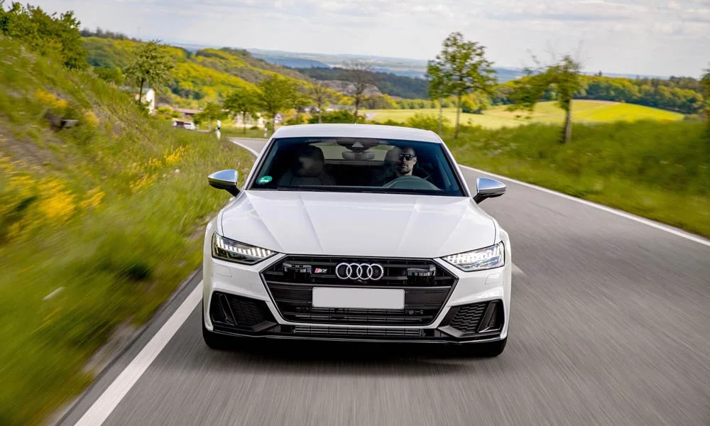 Фото Audi S7 Sportback — вид спереди, фото 5. Белый кузов, строгая симметрия оптики — базовый ракурс знакомства с дизайном. Дневные ходовые огни включаются автоматически с запуском Audi S7 Sportback — вид спереди, фото 5