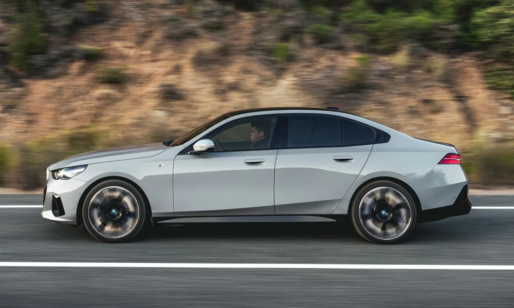 Фото BMW 5 серии (2024) — вид сбоку, фото 2. Профиль кузова: колёсная база, свесы и линия остекления. Хромированные или чёрные молдинги окон отличают комплектации BMW 5 серии (2024) — вид сбоку, фото 2