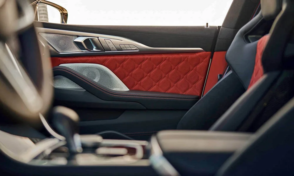 Фото BMW M8 Gran Coupe (2022) — дверная карта. Дверная карта в красно-чёрной отделке: подлокотник, динамик и блок стеклоподъёмников. Мягкая вставка в зоне локтя — то, что чувствуешь каждый день BMW M8 Gran Coupe (2022) — дверная карта