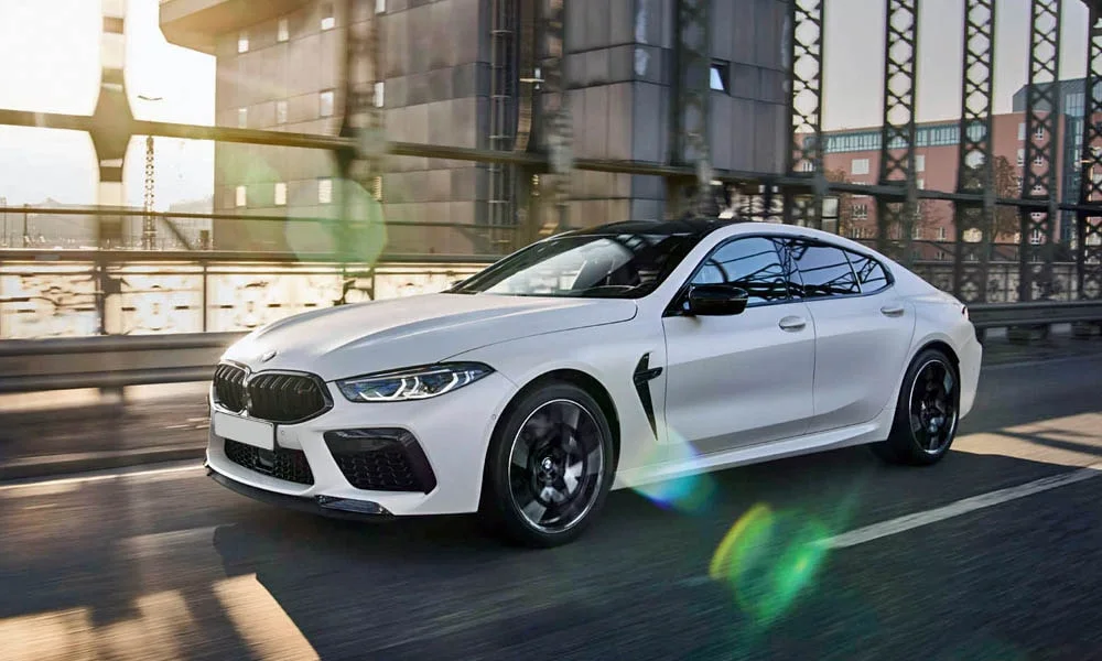 Фото BMW M8 Gran Coupe (2022) — вид спереди, фото 4. Передок в белом исполнении — крупная светотехника и выразительный бампер. Рисунок ходовых огней — подпись модели, по нему её узнают в потоке BMW M8 Gran Coupe (2022) — вид спереди, фото 4