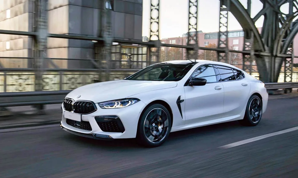 Фото BMW M8 Gran Coupe (2022) — вид спереди, фото 7. Передок в белом исполнении — крупная светотехника и выразительный бампер. Рисунок ходовых огней — подпись модели, по нему её узнают в потоке BMW M8 Gran Coupe (2022) — вид спереди, фото 7