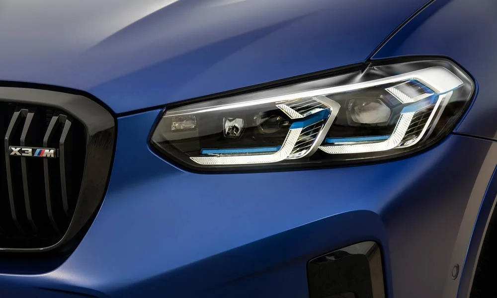 Фото BMW X3 M (2024) — вид спереди, фото 5. Кузов в синем цвете: рисунок оптики и решётки задаёт узнаваемое «лицо» модели. Рисунок ходовых огней — подпись модели, по нему её узнают в потоке BMW X3 M (2024) — вид спереди, фото 5
