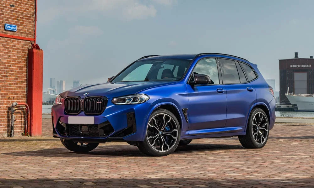 Фото BMW X3 M (2024) — вид спереди, фото 8. Передок в синем исполнении — крупная светотехника и выразительный бампер. Рисунок ходовых огней — подпись модели, по нему её узнают в потоке BMW X3 M (2024) — вид спереди, фото 8