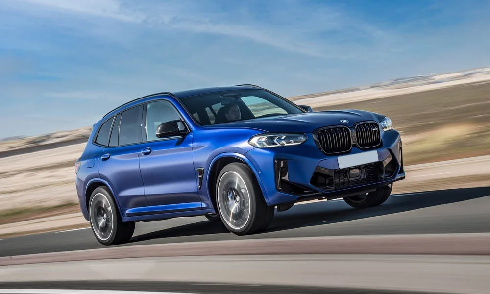 Фото BMW X3 M (2024) — вид спереди, фото 11. Передок в синем исполнении — крупная светотехника и выразительный бампер. Рисунок ходовых огней — подпись модели, по нему её узнают в потоке BMW X3 M (2024) — вид спереди, фото 11