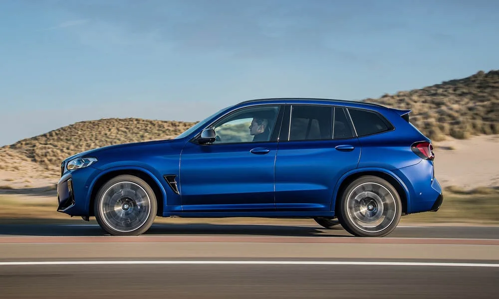 Фото BMW X3 M (2024) — вид сбоку, фото 3. Синий кузов в профиль — пропорции, высота посадки и дизайн дисков BMW X3 M (2024) — вид сбоку, фото 3