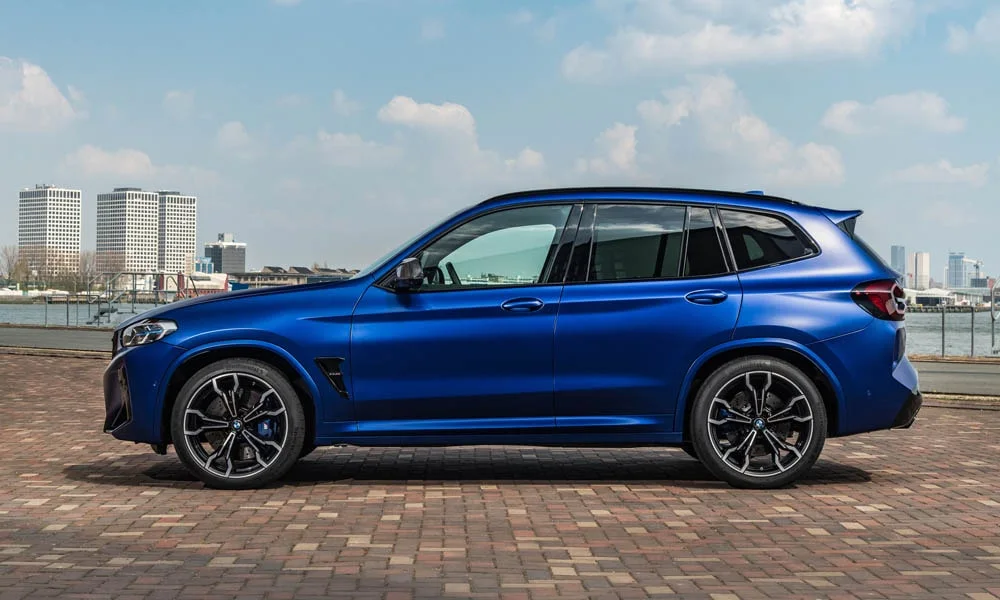 Фото BMW X3 M (2024) — вид сбоку, фото 4. Профиль в синем цвете: соотношение колёсной базы и свесов. Хромированные или чёрные молдинги окон отличают комплектации BMW X3 M (2024) — вид сбоку, фото 4