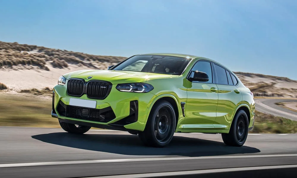 Фото BMW X4 M (2024) — вид спереди, фото 4. Зелёный кузов, строгая симметрия оптики — базовый ракурс знакомства с дизайном. Рисунок ходовых огней — подпись модели, по нему её узнают в потоке BMW X4 M (2024) — вид спереди, фото 4