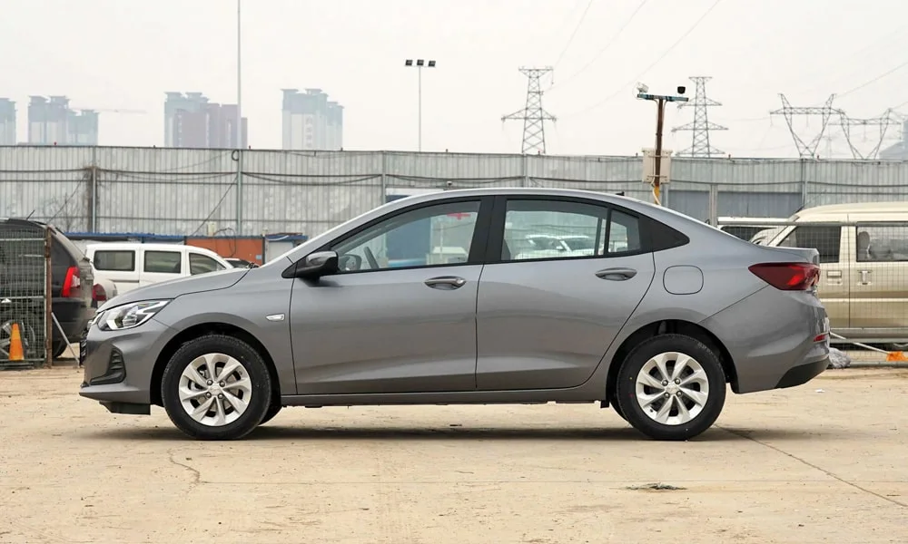 Фото Chevrolet Onix (2024) — вид сбоку, фото 2. Серый кузов в профиль — пропорции, высота посадки и дизайн дисков. Хромированные или чёрные молдинги окон отличают комплектации Chevrolet Onix (2024) — вид сбоку, фото 2