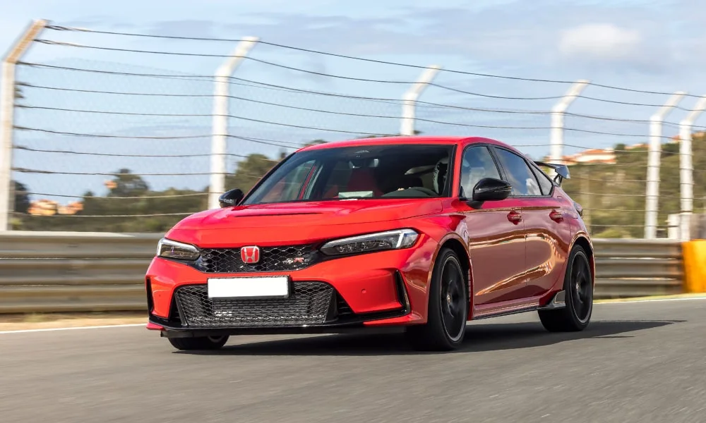Фото Honda Civic Type R (2024) — вид спереди, фото 8. Красный кузов, строгая симметрия оптики — базовый ракурс знакомства с дизайном. Дневные ходовые огни включаются автоматически с запуском Honda Civic Type R (2024) — вид спереди, фото 8
