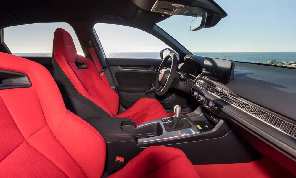 Фото Honda Civic Type R (2024) — интерьер. Салон в красно-чёрной отделке: архитектура передней панели, консоль и кресла. Светлая гамма зрительно расширяет салон, тёмная — практичнее в уходе Honda Civic Type R (2024) — интерьер