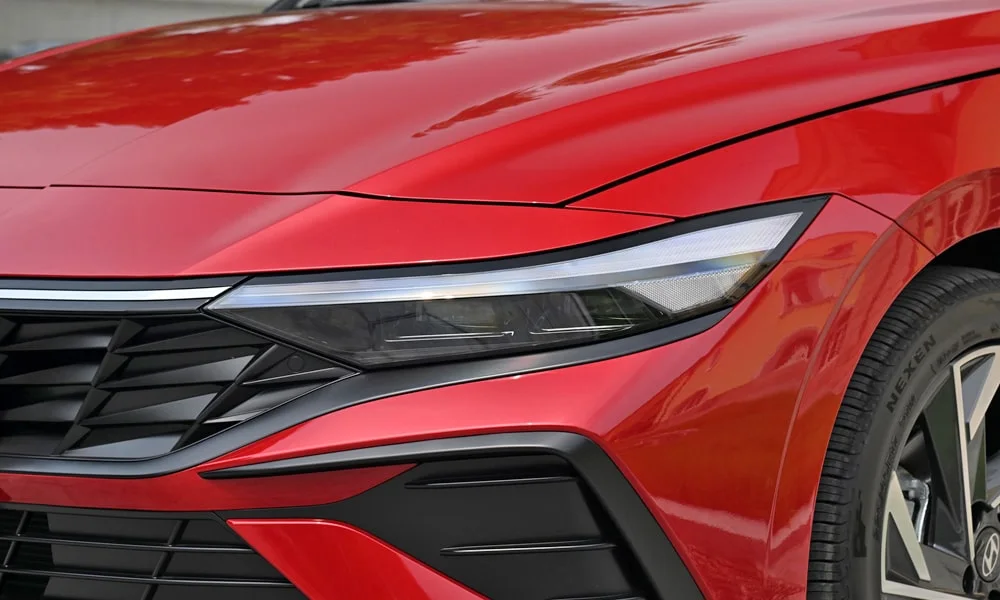 Фото Hyundai Elantra (2024) — вид спереди, фото 7. Кузов в красном цвете: рисунок оптики и решётки задаёт узнаваемое «лицо» модели. Дневные ходовые огни включаются автоматически с запуском Hyundai Elantra (2024) — вид спереди, фото 7