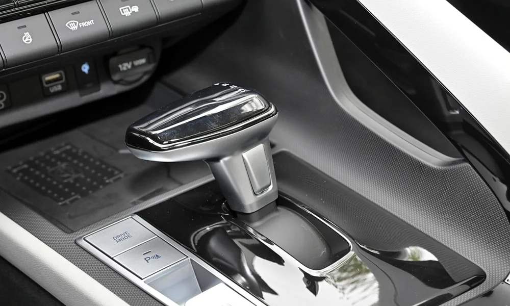 Фото Hyundai Elantra (2024) — селектор коробки передач. Селектор трансмиссии на центральной консоли. Режимы движения и электронный ручник собраны рядом с селектором Hyundai Elantra (2024) — селектор коробки передач