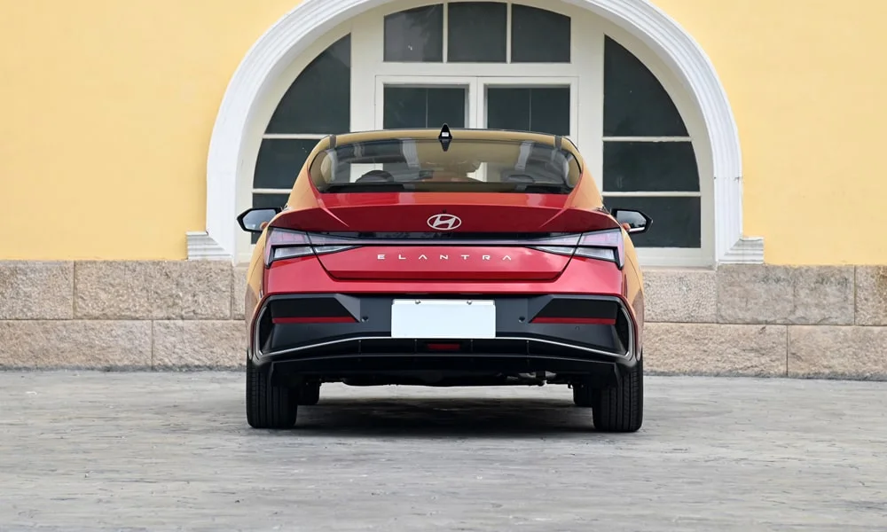 Фото Hyundai Elantra (2024) — вид сзади, фото 5. Линия крыши, стойки и задняя дверь в красном исполнении. Насадки выхлопа или их имитация внизу бампера различают версии Hyundai Elantra (2024) — вид сзади, фото 5