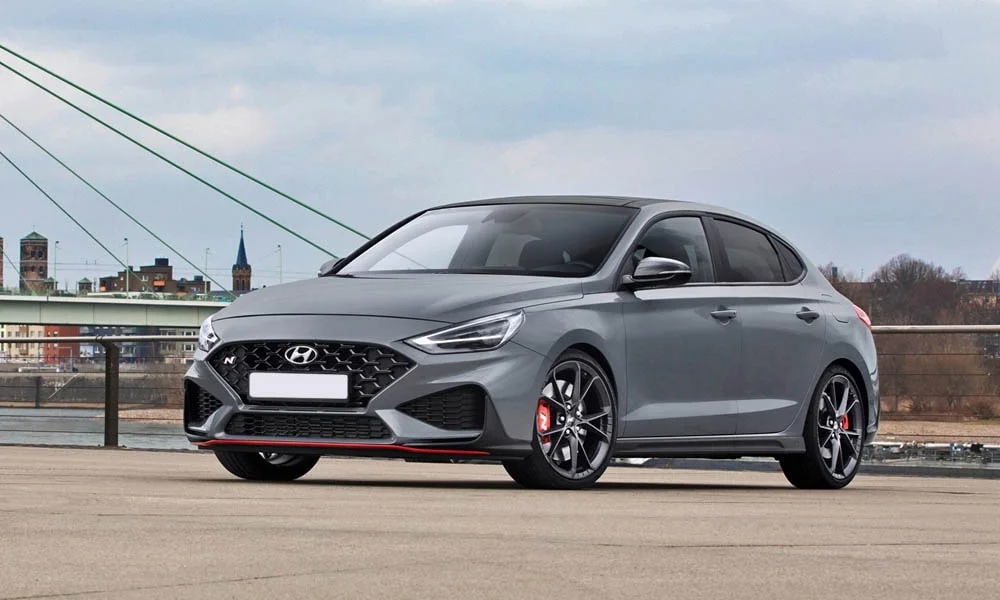 Фото Hyundai i30 Fastback N (2024) — вид спереди, фото 5. Передок в сером исполнении — крупная светотехника и выразительный бампер. Рисунок ходовых огней — подпись модели, по нему её узнают в потоке Hyundai i30 Fastback N (2024) — вид спереди, фото 5