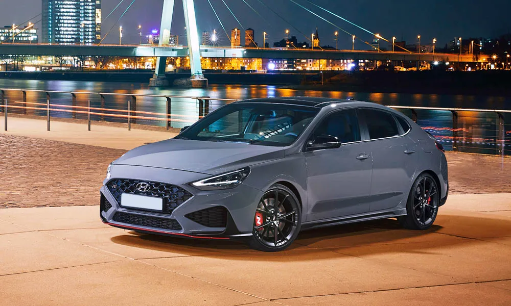 Фото Hyundai i30 Fastback N (2024) — вид спереди, фото 10. Серый кузов, строгая симметрия оптики — базовый ракурс знакомства с дизайном. Дневные ходовые огни включаются автоматически с запуском Hyundai i30 Fastback N (2024) — вид спереди, фото 10