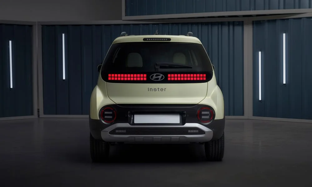 Фото Hyundai Inster — вид сзади, фото 8. Бежевый кузов сзади — фонари и бампер определяют ночной образ модели. Насадки выхлопа или их имитация внизу бампера различают версии Hyundai Inster — вид сзади, фото 8