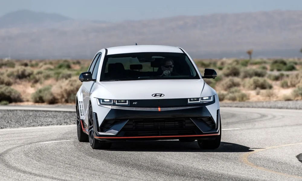 Фото Hyundai IONIQ 5 N — вид спереди, фото 8. Белый кузов, строгая симметрия оптики — базовый ракурс знакомства с дизайном. Рисунок ходовых огней — подпись модели, по нему её узнают в потоке Hyundai IONIQ 5 N — вид спереди, фото 8