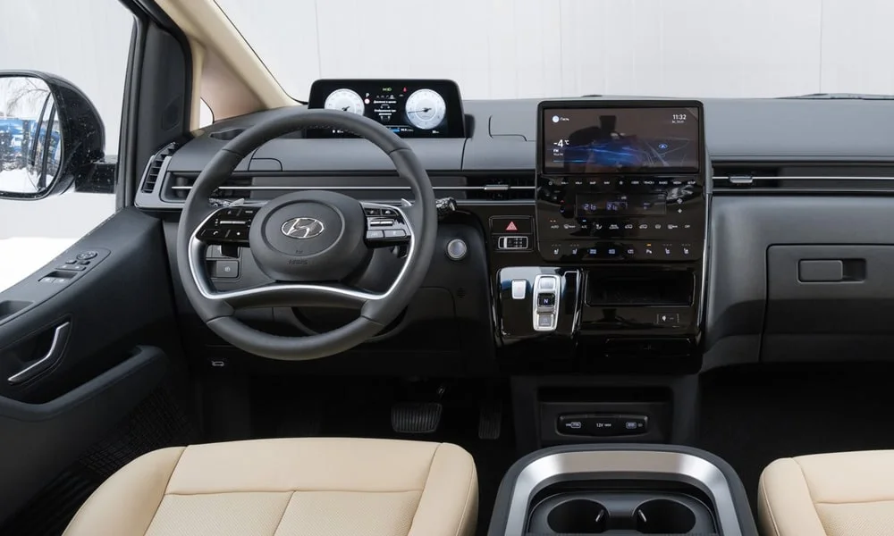 Фото Hyundai Staria (2022) — передняя панель. Панель в светлой бежевой отделке — видна компоновка экранов и органов управления. Мягкие материалы верхнего яруса и вставки задают уровень интерьера Hyundai Staria (2022) — передняя панель