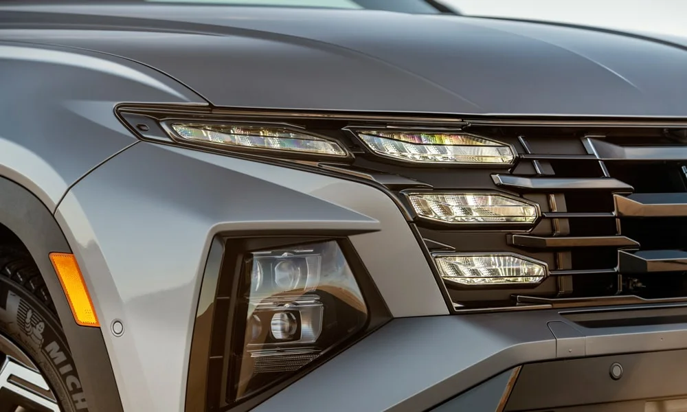 Фото Hyundai Tucson (2024) — вид спереди, фото 5. Кузов в сером цвете: рисунок оптики и решётки задаёт узнаваемое «лицо» модели. Дневные ходовые огни включаются автоматически с запуском Hyundai Tucson (2024) — вид спереди, фото 5