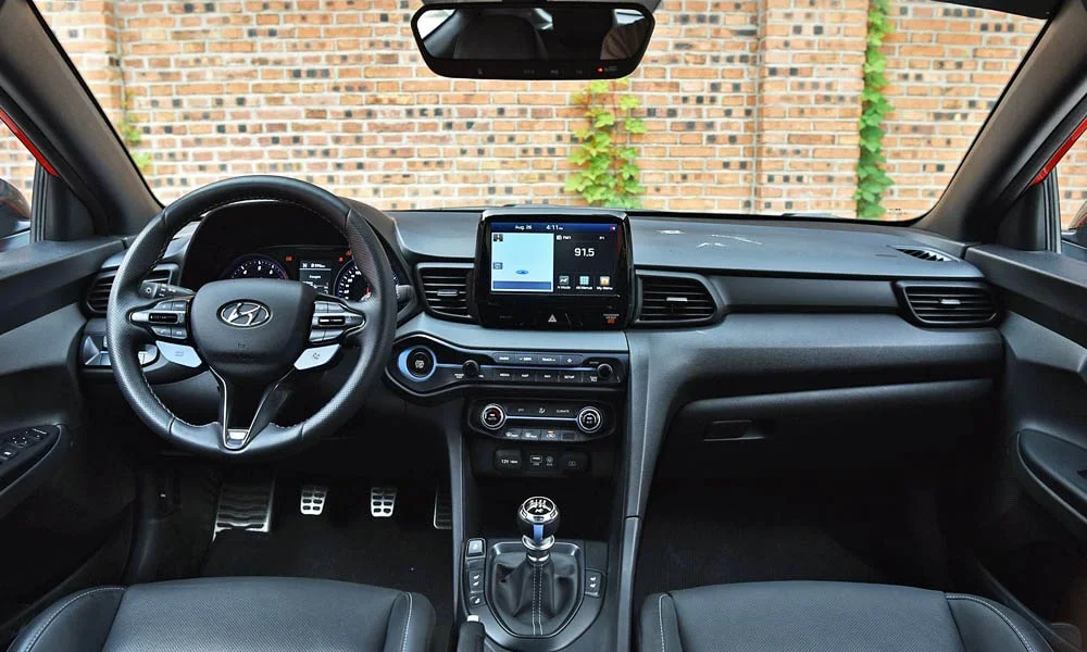 Фото Hyundai Veloster N (2024) — передняя панель. Передняя панель в красно-чёрной отделке: расположение экранов и дефлекторов. Мягкие материалы верхнего яруса и вставки задают уровень интерьера Hyundai Veloster N (2024) — передняя панель