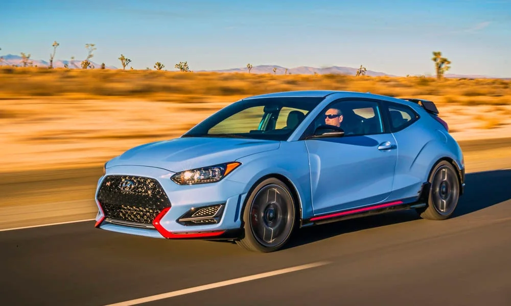 Фото Hyundai Veloster N (2024) — вид спереди, фото 8. Кузов в синем цвете: рисунок оптики и решётки задаёт узнаваемое «лицо» модели. Рисунок ходовых огней — подпись модели, по нему её узнают в потоке Hyundai Veloster N (2024) — вид спереди, фото 8