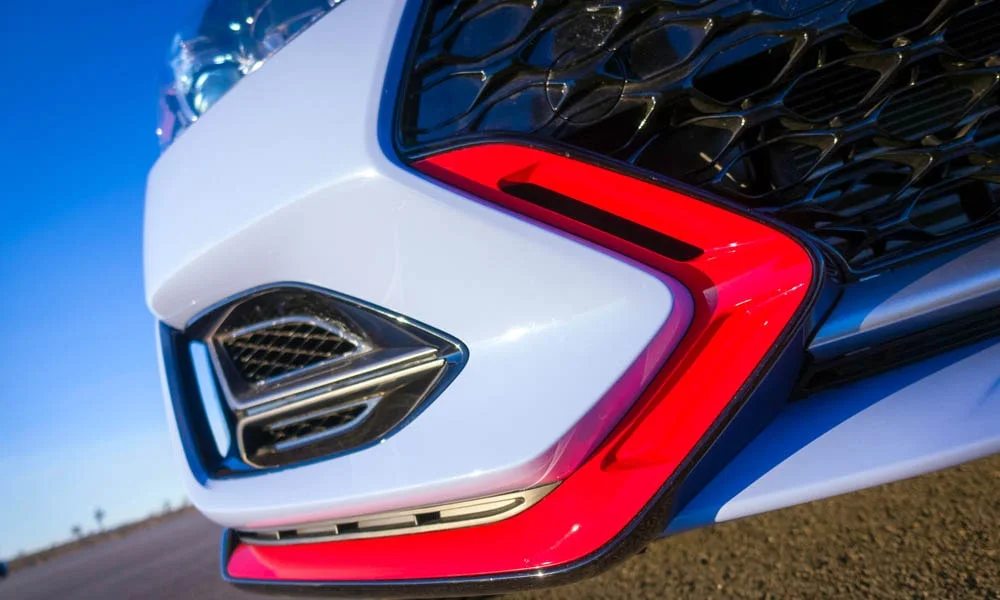 Фото Hyundai Veloster N (2024) — вид спереди, фото 10. Белый кузов, строгая симметрия оптики — базовый ракурс знакомства с дизайном. Рисунок ходовых огней — подпись модели, по нему её узнают в потоке Hyundai Veloster N (2024) — вид спереди, фото 10