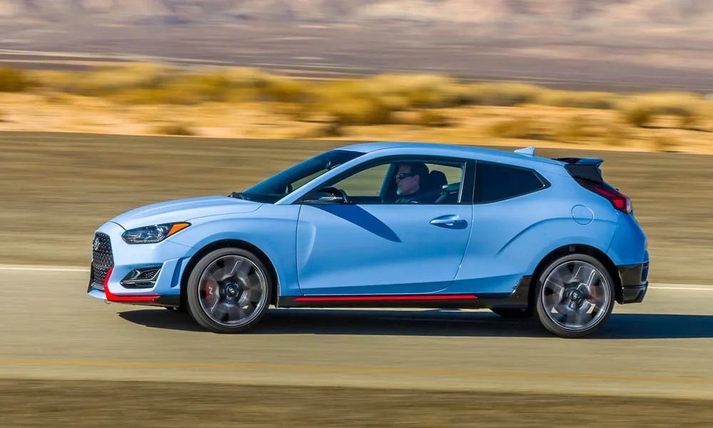 Фото Hyundai Veloster N (2024) — вид сбоку, фото 3. Профиль в синем цвете: соотношение колёсной базы и свесов. Длинная база — простор второго ряда; короткие свесы упрощают парковку Hyundai Veloster N (2024) — вид сбоку, фото 3