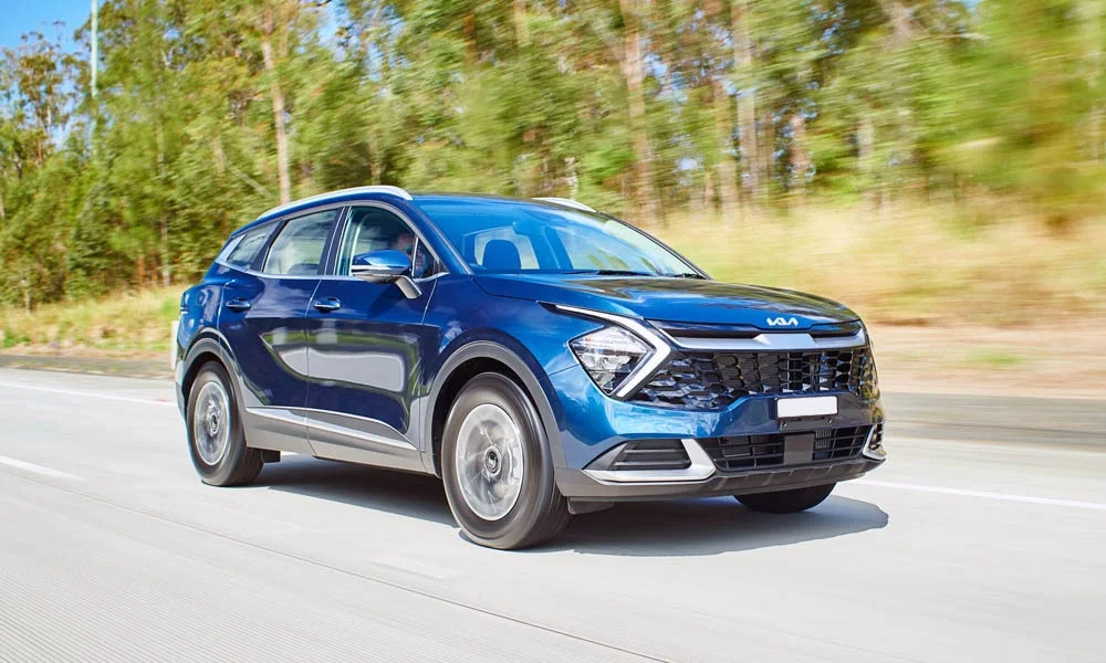 Фото KIA Sportage (2022) — вид спереди, фото 9. Синий кузов, строгая симметрия оптики — базовый ракурс знакомства с дизайном. Рисунок ходовых огней — подпись модели, по нему её узнают в потоке KIA Sportage (2022) — вид спереди, фото 9