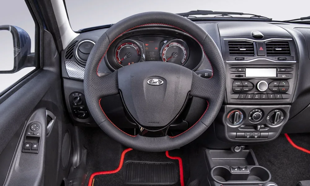 Фото LADA Granta Sportline Лифтбек (2023) — передняя панель. Архитектура передней панели: ярусы, вставки и консоль в красно-чёрной гамме. Мягкие материалы верхнего яруса и вставки задают уровень интерьера LADA Granta Sportline Лифтбек (2023) — передняя панель