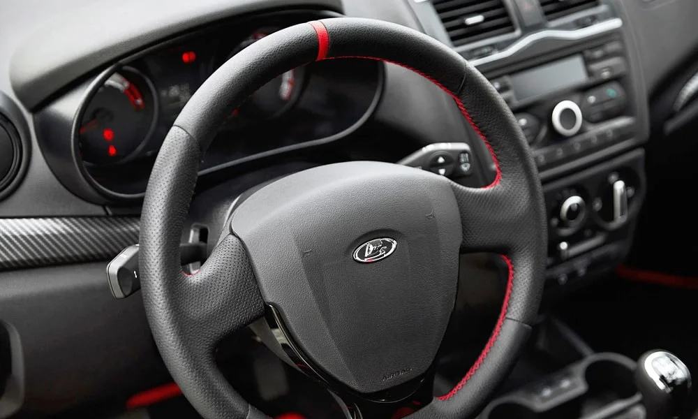 Фото LADA Granta Sport (2023) — руль, фото 2. Обшивка обода и компоновка спиц крупным планом. Клавиши на спицах управляют медиа, круизом и ассистентами — руки остаются на руле LADA Granta Sport (2023) — руль, фото 2