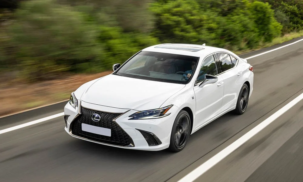 Фото Lexus ES 350 — вид спереди, фото 7. Белый кузов, строгая симметрия оптики — базовый ракурс знакомства с дизайном. Рисунок ходовых огней — подпись модели, по нему её узнают в потоке Lexus ES 350 — вид спереди, фото 7