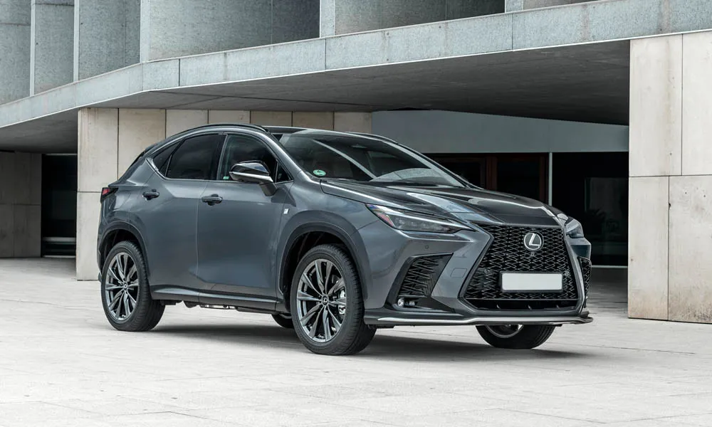 Фото Lexus NX 450h (2024) — вид спереди. Кузов в сером цвете: рисунок оптики и решётки задаёт узнаваемое «лицо» модели. Рисунок ходовых огней — подпись модели, по нему её узнают в потоке Lexus NX 450h (2024) — вид спереди
