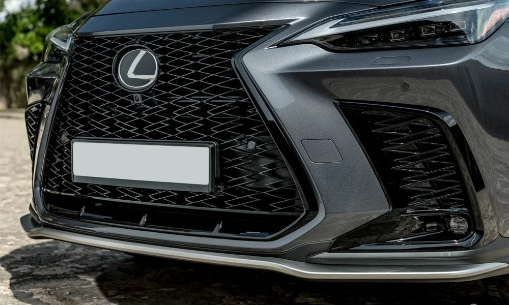 Фото Lexus NX 450h (2024) — решётка радиатора. Фирменный рисунок облицовки — визитная карточка марки. За решёткой у многих комплектаций стоит радар адаптивного круиз-контроля Lexus NX 450h (2024) — решётка радиатора
