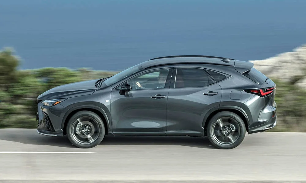Фото Lexus NX 450h (2024) — вид сбоку, фото 2. Серый кузов в профиль — пропорции, высота посадки и дизайн дисков. Хромированные или чёрные молдинги окон отличают комплектации Lexus NX 450h (2024) — вид сбоку, фото 2