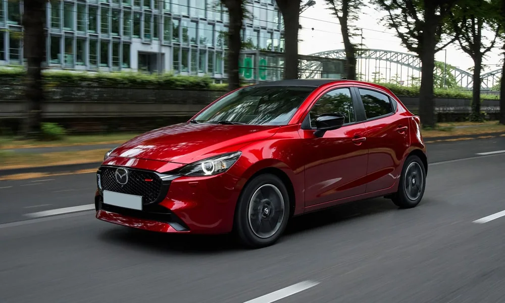 Фото Mazda 2 (2024) — вид спереди, фото 5. Передок в красном исполнении — крупная светотехника и выразительный бампер. Рисунок ходовых огней — подпись модели, по нему её узнают в потоке Mazda 2 (2024) — вид спереди, фото 5