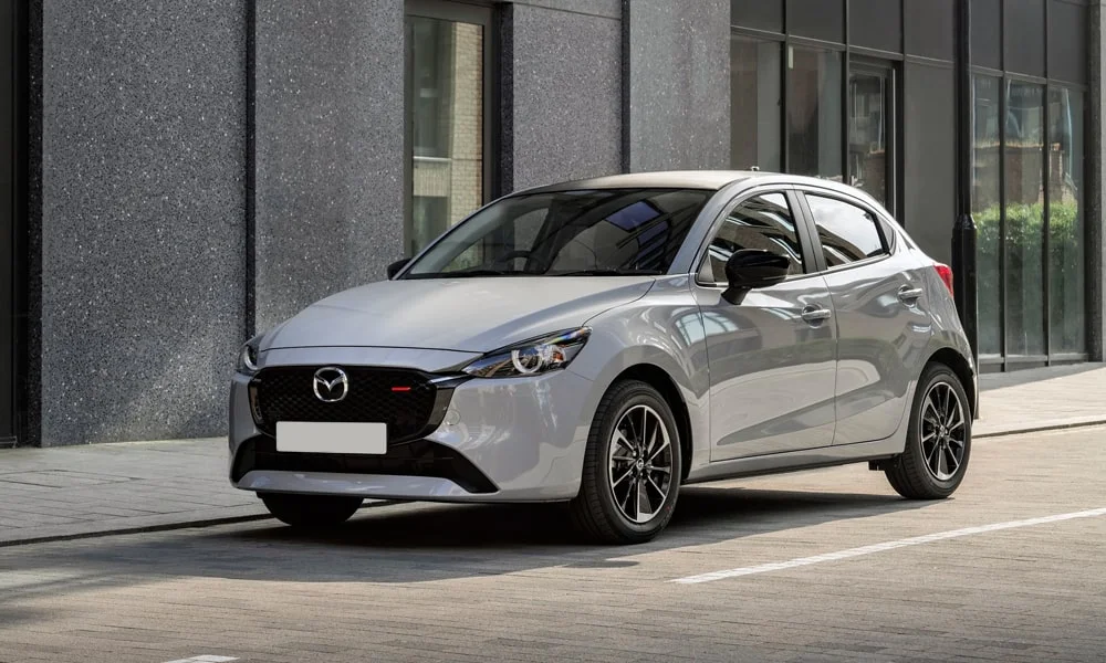 Фото Mazda 2 (2024) — вид спереди, фото 9. Передок в серебристом исполнении — крупная светотехника и выразительный бампер. Рисунок ходовых огней — подпись модели, по нему её узнают в потоке Mazda 2 (2024) — вид спереди, фото 9