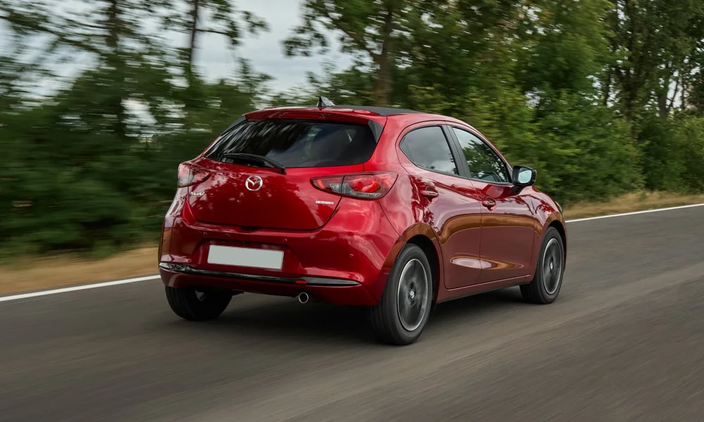 Фото Mazda 2 (2024) — вид сзади, фото 2. Корма в красном цвете: графика фонарей и пластика пятой двери. Насадки выхлопа или их имитация внизу бампера различают версии Mazda 2 (2024) — вид сзади, фото 2