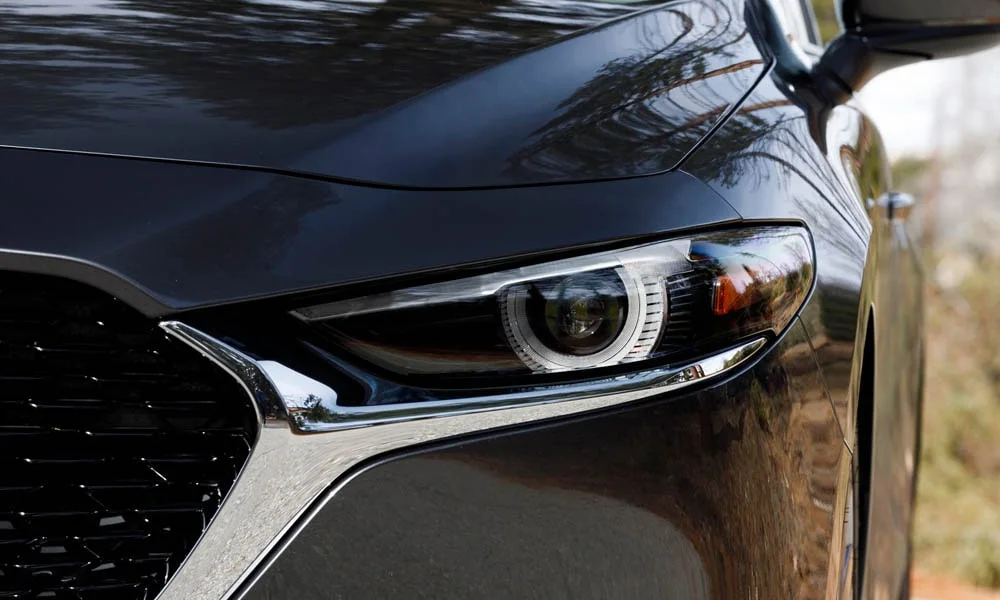 Фото Mazda 3 — вид спереди, фото 17. Кузов в чёрном цвете: рисунок оптики и решётки задаёт узнаваемое «лицо» модели. Дневные ходовые огни включаются автоматически с запуском Mazda 3 — вид спереди, фото 17