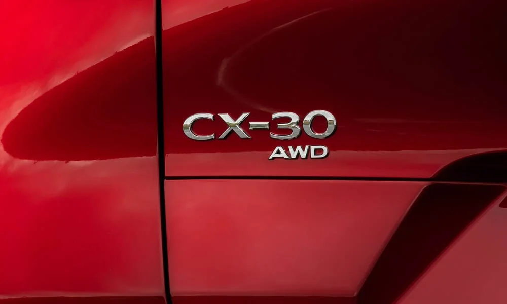 Фото Mazda CX-30 — эмблема. Логотип марки крупным планом. Шильдик версии на корме помогает отличать комплектации Mazda CX-30 — эмблема