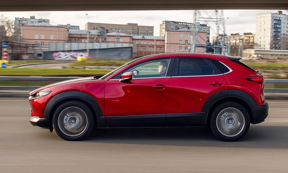 Фото Mazda CX-30 — вид сбоку, фото 2. Сбоку читаются линия остекления и характер выштамповок на красном кузове. Длинная база — простор второго ряда; короткие свесы упрощают парковку Mazda CX-30 — вид сбоку, фото 2