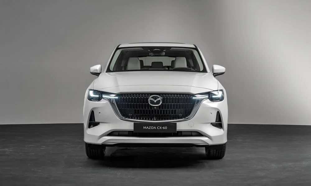 Фото Mazda CX-60 (2024) — вид спереди, фото 6. Кузов в белом цвете: рисунок оптики и решётки задаёт узнаваемое «лицо» модели. Дневные ходовые огни включаются автоматически с запуском Mazda CX-60 (2024) — вид спереди, фото 6