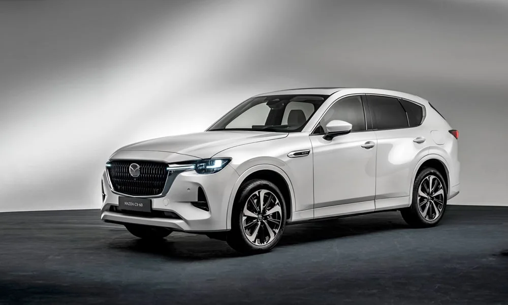 Фото Mazda CX-60 (2024) — вид спереди, фото 7. Кузов в белом цвете: рисунок оптики и решётки задаёт узнаваемое «лицо» модели. Рисунок ходовых огней — подпись модели, по нему её узнают в потоке Mazda CX-60 (2024) — вид спереди, фото 7