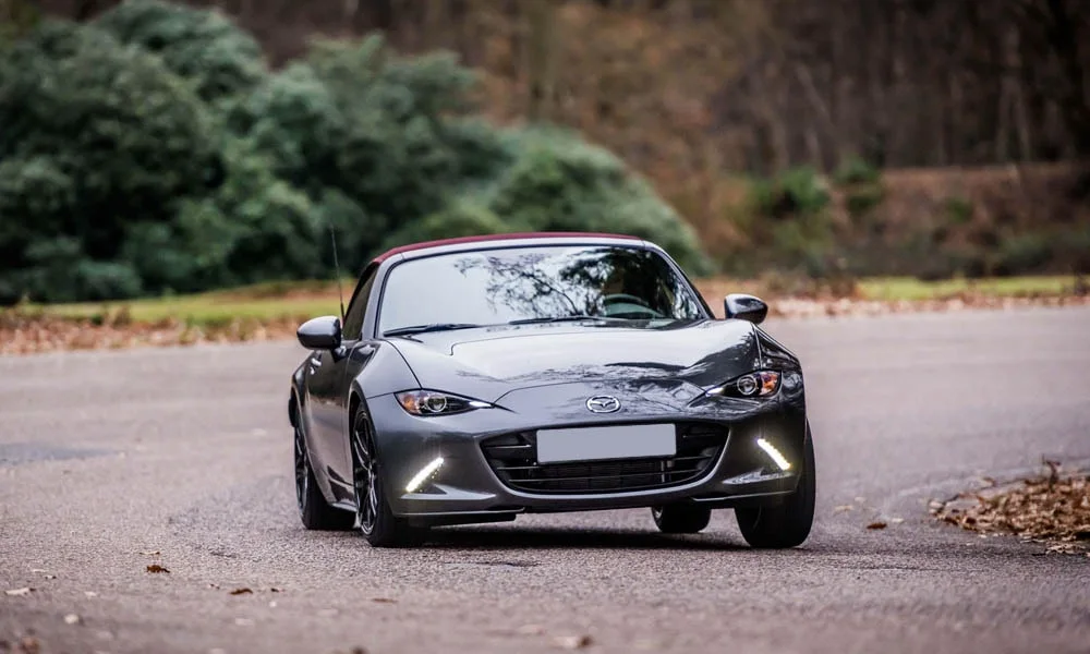 Фото Mazda MX-5 — вид спереди, фото 4. Передок в чёрном исполнении — крупная светотехника и выразительный бампер. Дневные ходовые огни включаются автоматически с запуском Mazda MX-5 — вид спереди, фото 4