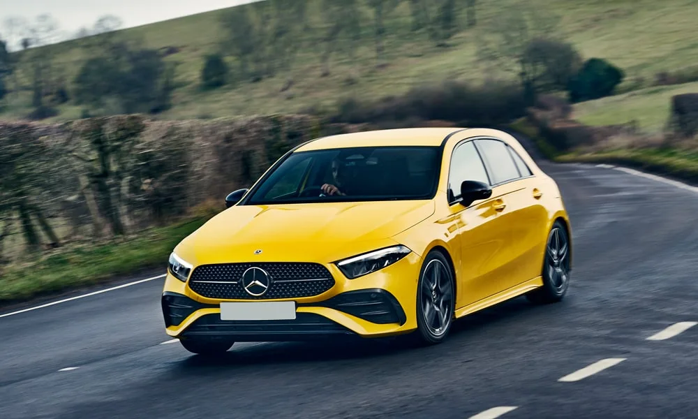 Фото Mercedes-Benz A-Class (2024) — вид спереди, фото 5. Жёлтый кузов, строгая симметрия оптики — базовый ракурс знакомства с дизайном. Рисунок ходовых огней — подпись модели, по нему её узнают в потоке Mercedes-Benz A-Class (2024) — вид спереди, фото 5