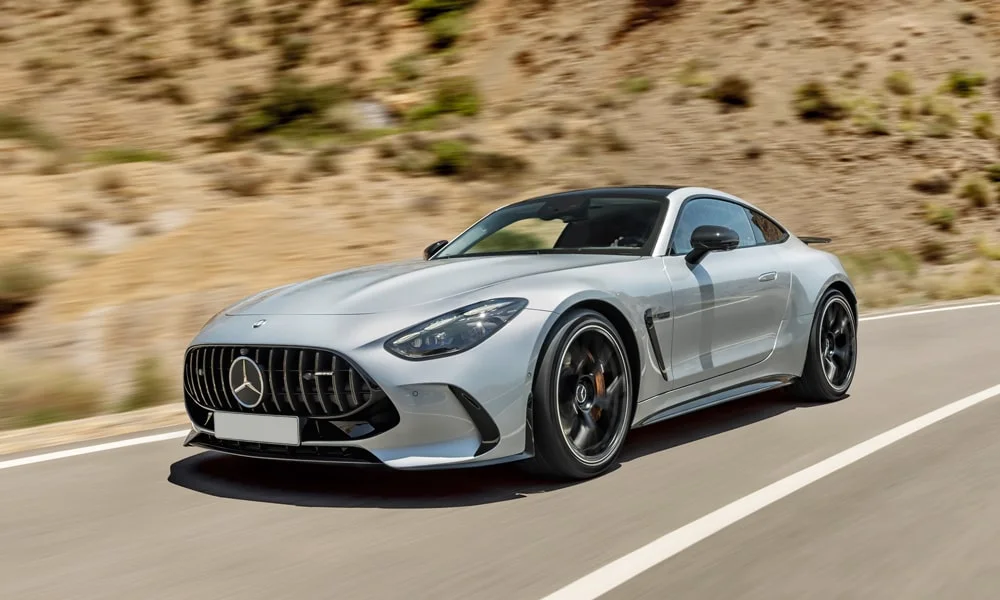 Фото Mercedes-Benz AMG GT (2024) — вид спереди, фото 10. Передок в серебристом исполнении — крупная светотехника и выразительный бампер. Рисунок ходовых огней — подпись модели, по нему её узнают в потоке Mercedes-Benz AMG GT (2024) — вид спереди, фото 10