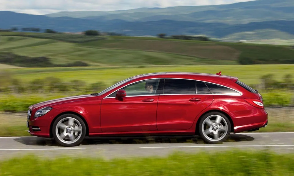Фото Mercedes-Benz CLS — вид сбоку. Сбоку читаются линия остекления и характер выштамповок на красном кузове Mercedes-Benz CLS — вид сбоку