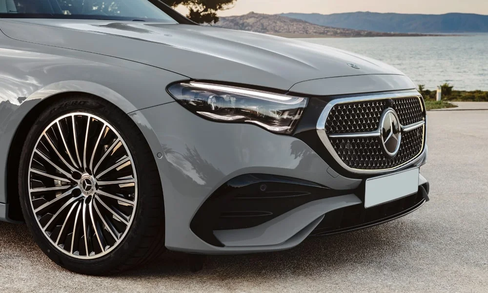 Фото Mercedes-Benz E-Class (2024) — вид спереди, фото 37. Кузов в сером цвете: рисунок оптики и решётки задаёт узнаваемое «лицо» модели. Рисунок ходовых огней — подпись модели, по нему её узнают в потоке Mercedes-Benz E-Class (2024) — вид спереди, фото 37
