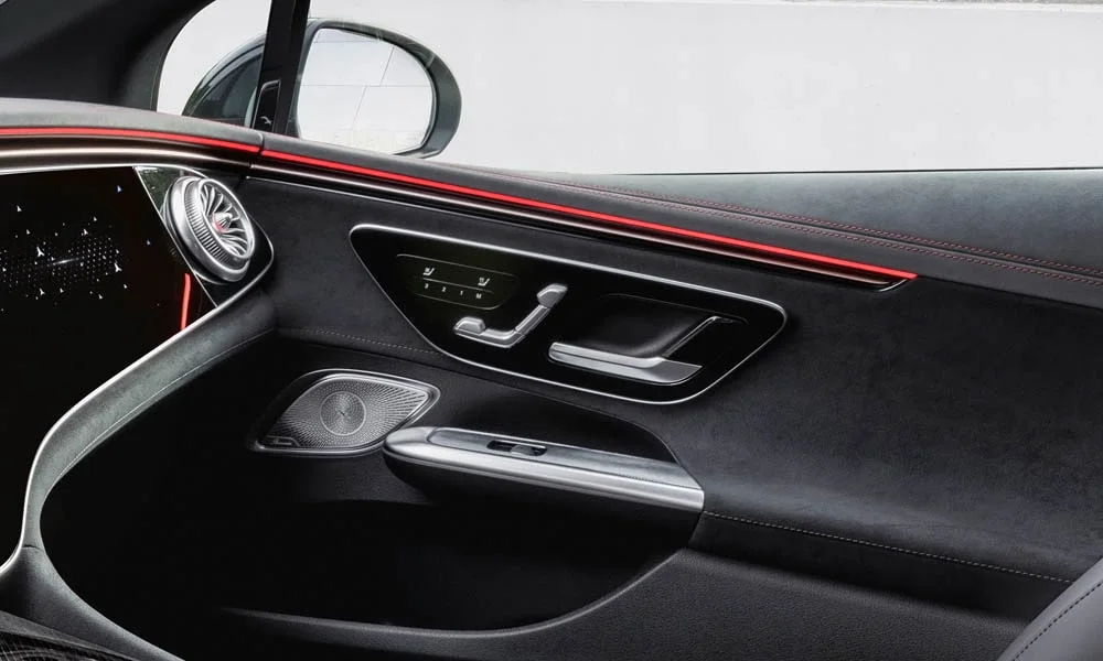 Фото Mercedes-Benz EQE (2024) — дверная карта. Дверная карта в красно-чёрной отделке: подлокотник, динамик и блок стеклоподъёмников. Решётка динамика в двери — часть штатной акустики Mercedes-Benz EQE (2024) — дверная карта