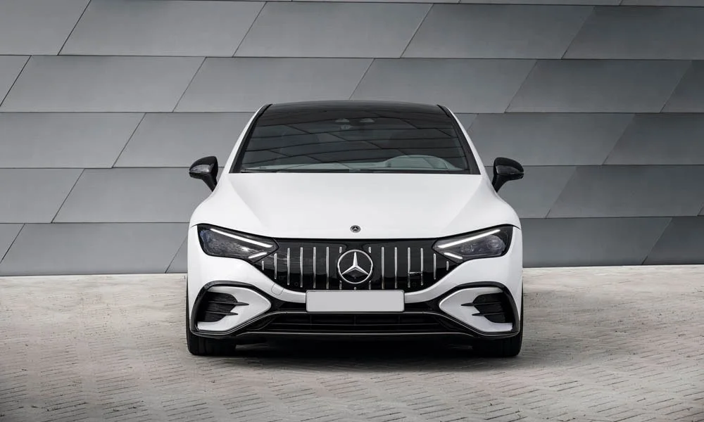 Фото Mercedes-Benz EQE (2024) — вид спереди, фото 4. Кузов в белом цвете: рисунок оптики и решётки задаёт узнаваемое «лицо» модели. Рисунок ходовых огней — подпись модели, по нему её узнают в потоке Mercedes-Benz EQE (2024) — вид спереди, фото 4